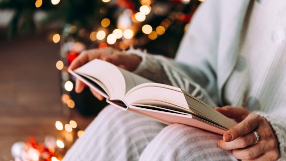 Article Image for a Happy Christmas Print (IPA Christmas Consumer Study): young woman is reading a book sitting by the Christmas tree.